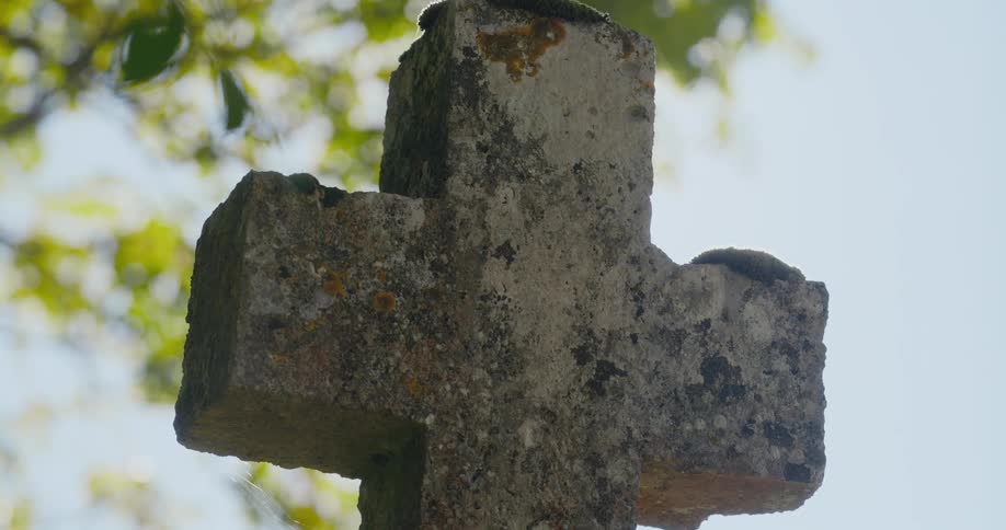 The sun shines brightly upon on a cross shaped gravestone