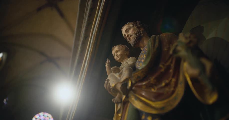 Richly detailed religious statue stands in high vaulted cathedral decorated with stained glass windows