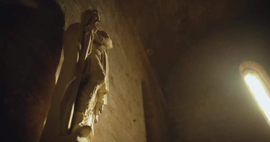 A sculpture mounted on a wall inside of a stone building during the day