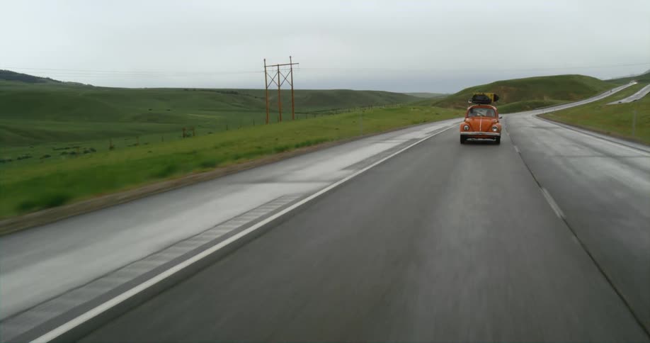 Volkswagen bug drives along highway through hill country