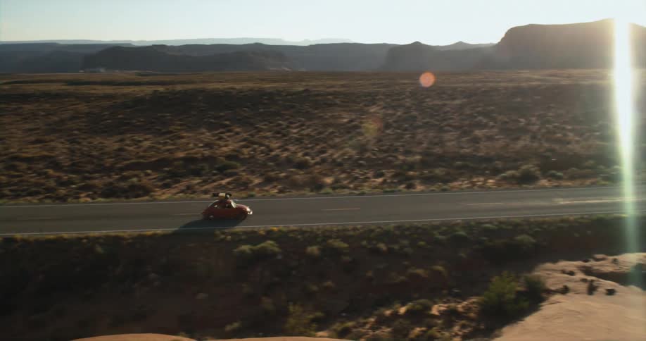 A vehicle travels along a road through a vast shrubland during the day