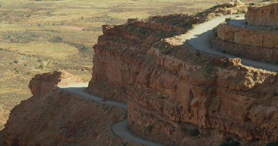A car travels along a mountain pass running along a butte in the badlands during the day