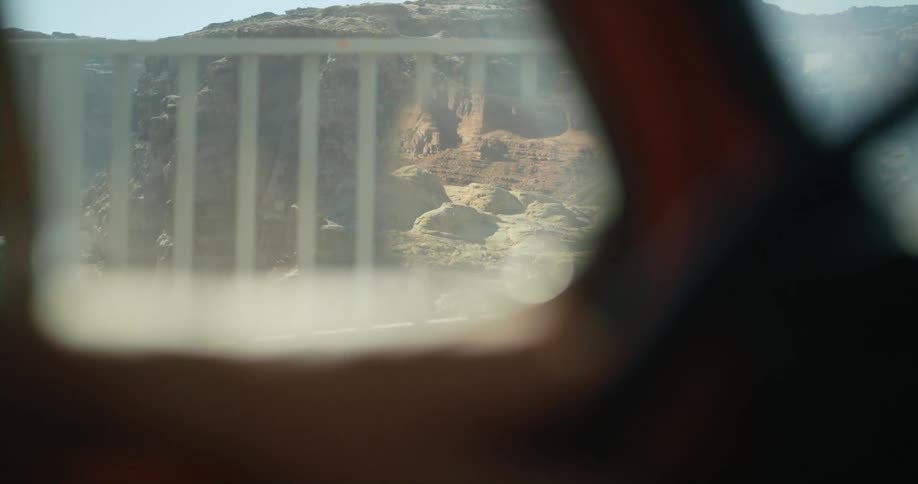Side mirror reflects badlands as vehicle moves over bridge over river