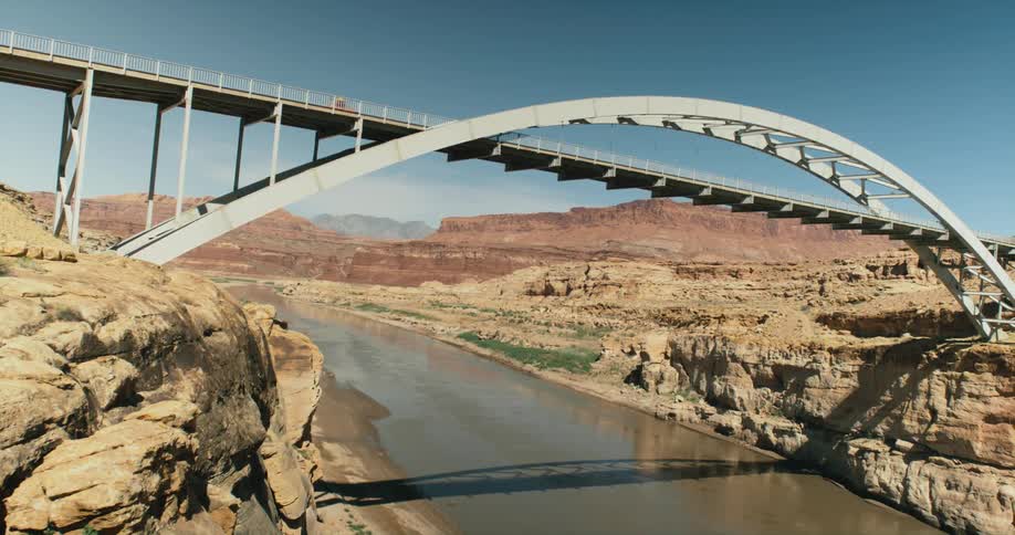 A vehicle travels along a bridge spanning a river in the an arid countryside during the day