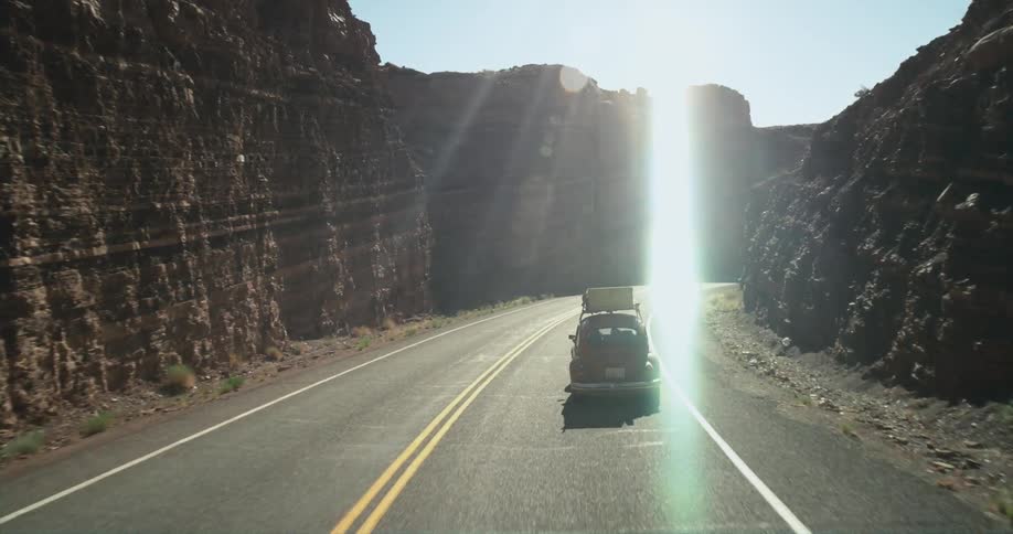 A volkswagen bug is traveling on a rural highway surrounded by rock cliffs
