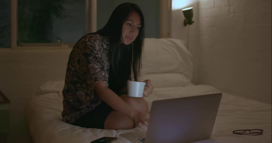 A woman drinks from a mug while using her laptop