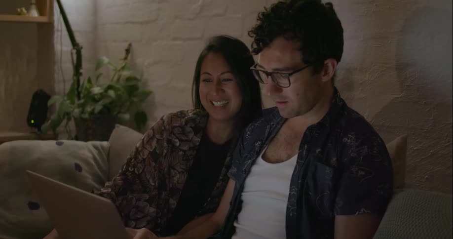 Man and woman sit on a couch talking and looking at a laptop