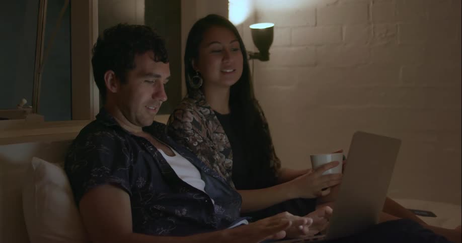 Man and woman sit on a couch talking and looking at a laptop