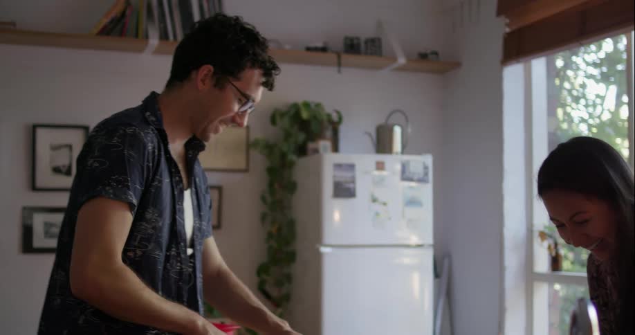 A man is cutting vegetables, laughing and talking with a woman