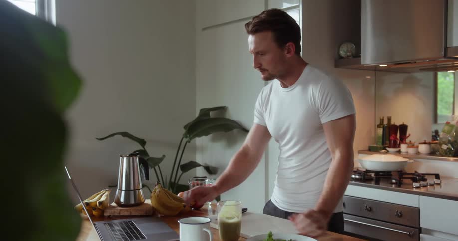 A man sips from a glass and uses a laptop