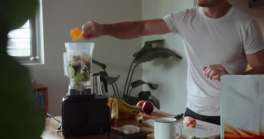 A man scoops some powder from a bag and adds it to the blender