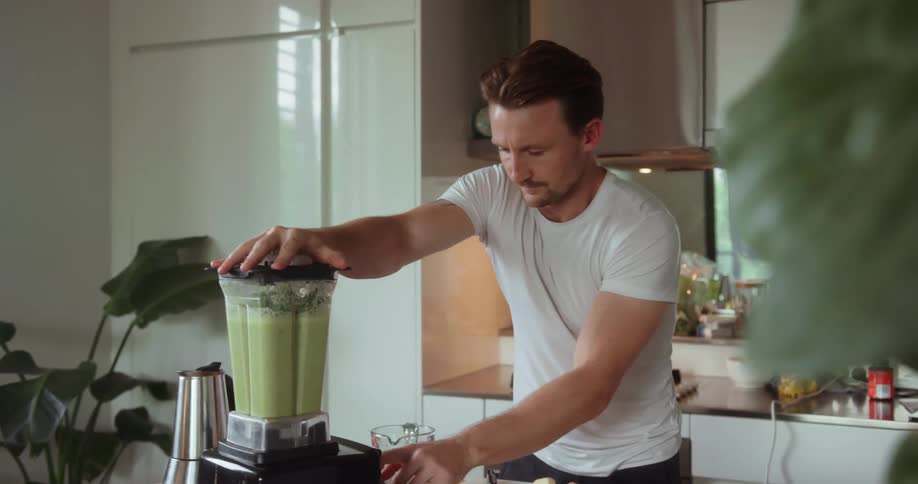 A man adds some greens to the blender and turns it on