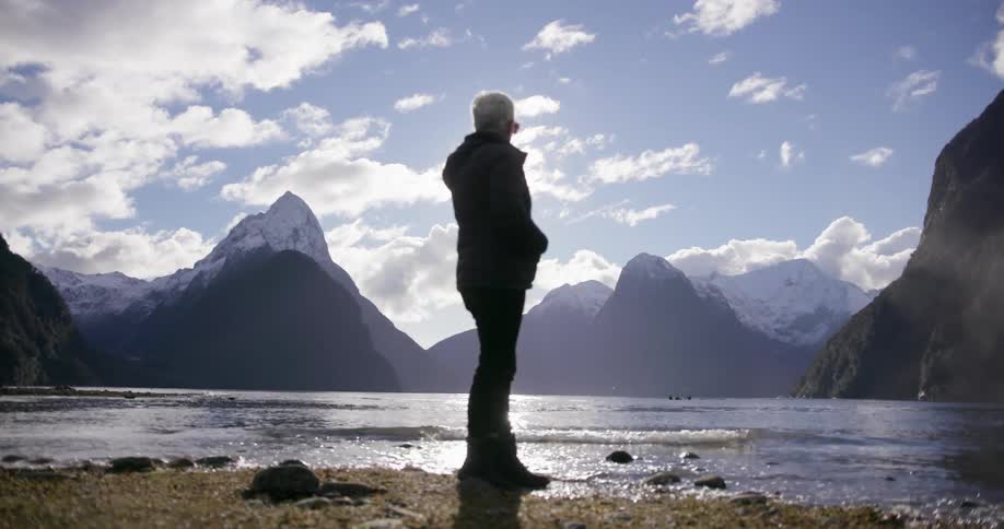 A woman stands in front of a flowing lake in front of mountains