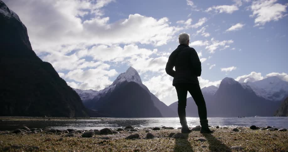 A woman stands in front of a flowing lake in front of mountains