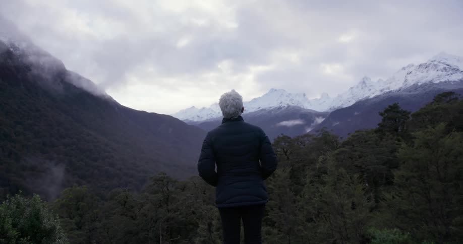 A person is standing on a hillside looking over a mountain range