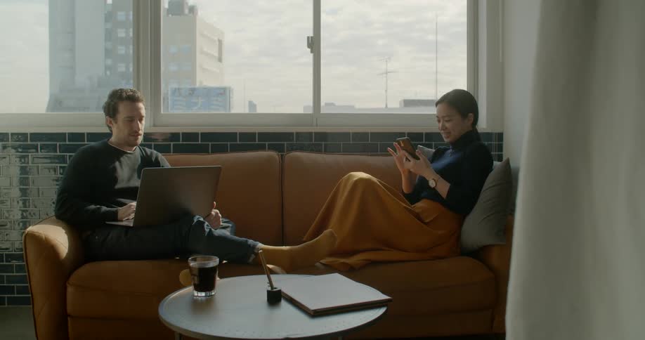 A man uses a laptop while sitting on a couch next to a woman using a smartphone