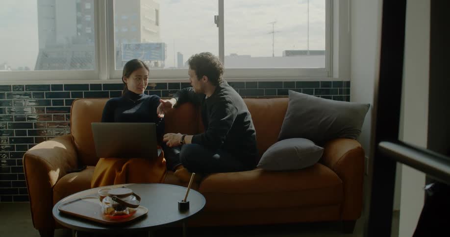 Couple sit on couch talking and viewing laptop