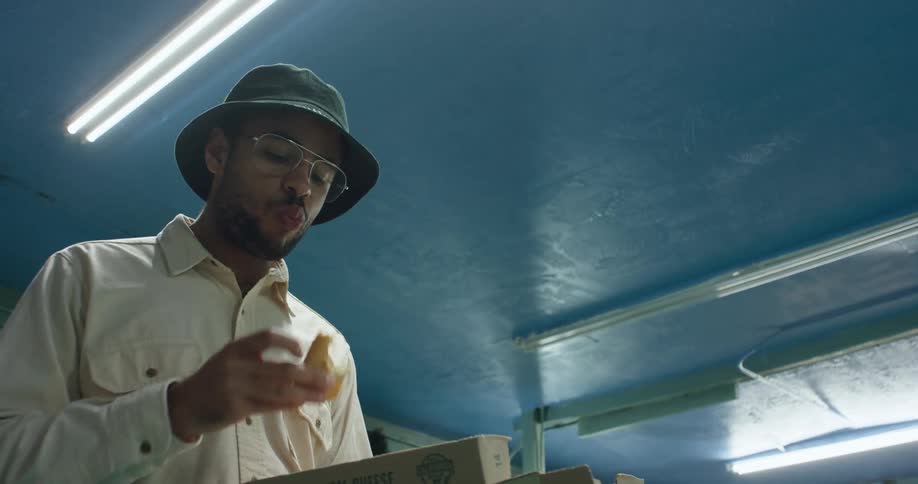 A man eats pizza directly from the box while indoors