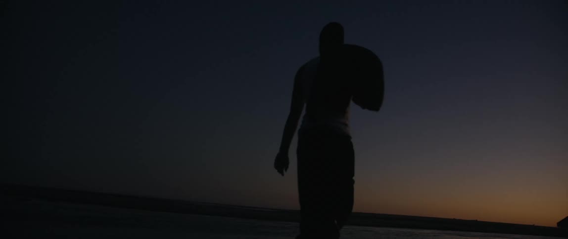 Silhouette of a man walking near the water on a beach and carrying a jacket over his shoulder