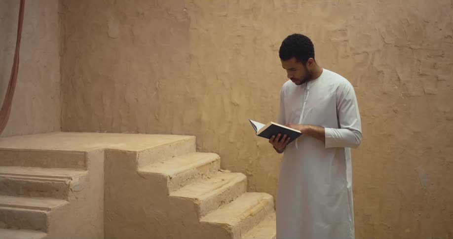A man in a white robe reads a religious book