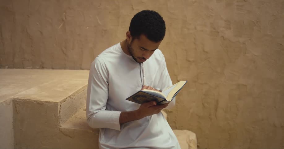 A young priest sits on stairs and reads a book