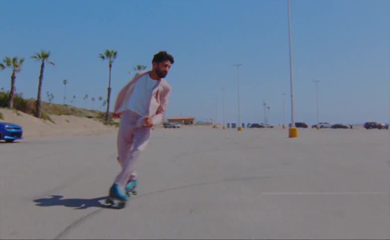 A man wearing a pink jacket and pants is dancing on roller skates in a parking lot
