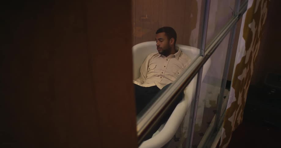 A depressed man lies in an empty bathtub in a bathroom