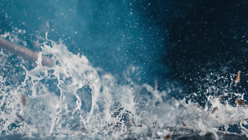 A hammer hits a bottle of beer on a table and shatters it as beer flies everywhere