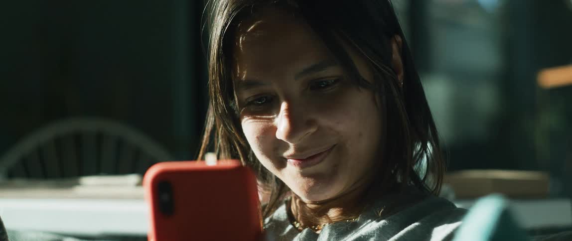A teenage girl is outside holding her cell phone and smiling