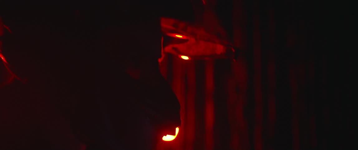 The silhouette of a person wearing a helmet and lowering the visor with a red light glowing behind