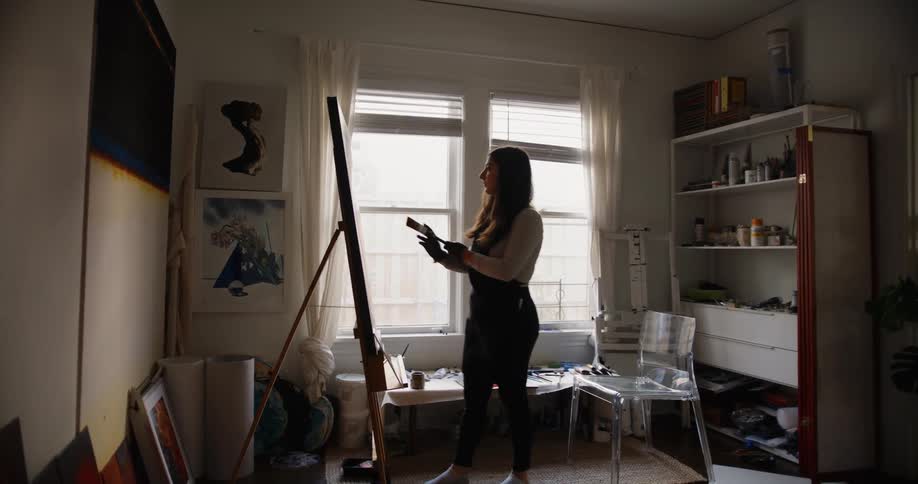 A young woman paints on a canvas at home