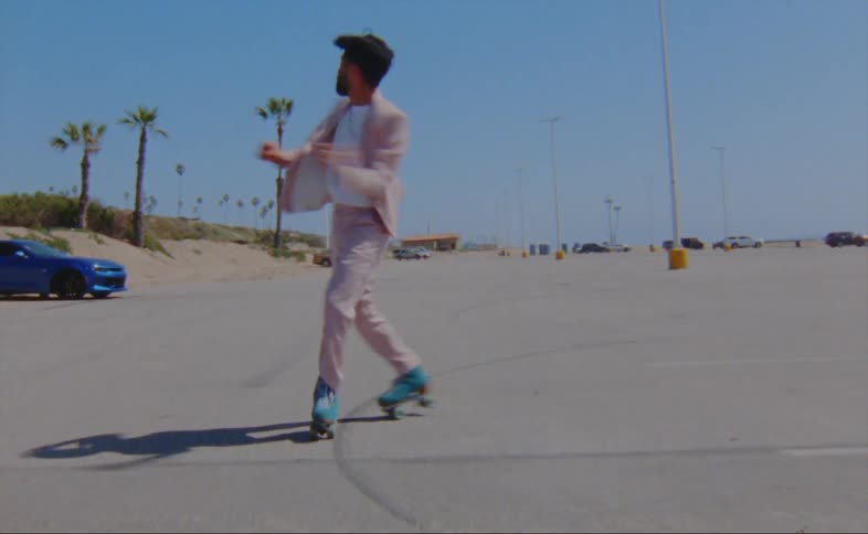 Man on turquois roller skates with beard white shirt and pink suit moves over a hard surface