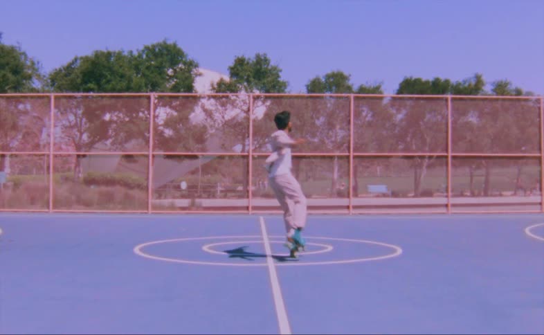 A man wearing a pink jacket and pants is figure skating on an outdoor basketball court