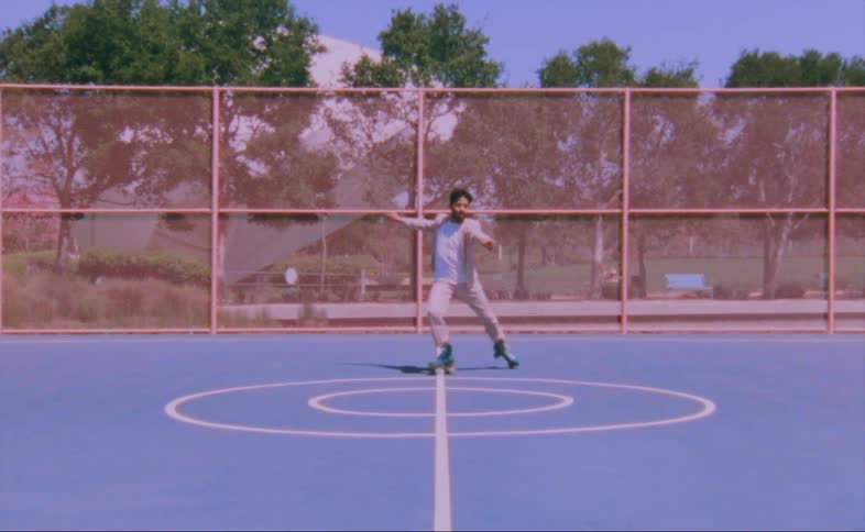 A man dances on roller skates on an outdoor basketball court during the day