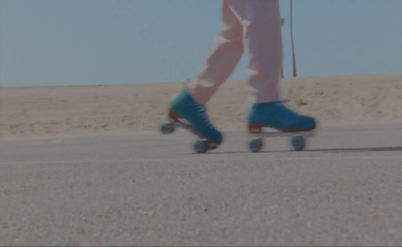 Person wearing pink dances on roller skates on asphalt near sandy area
