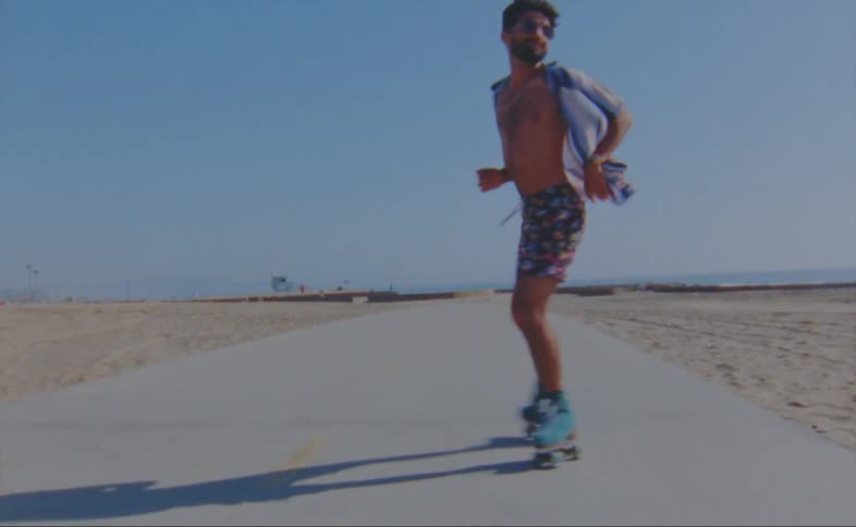 A man dances while roller skating down a path on a beach during the day