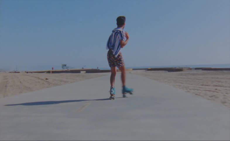 A man dances while skating down a path on a beach on a sunny day