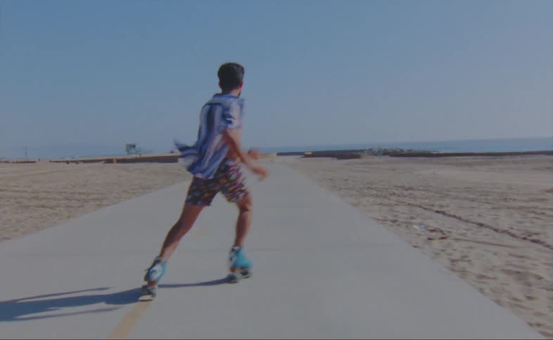 A man dances while roller skating down a walkway on the beach