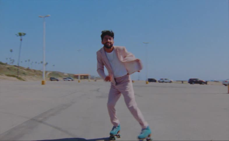 A man dances while roller skating through an outdoor parking lot on a clear day