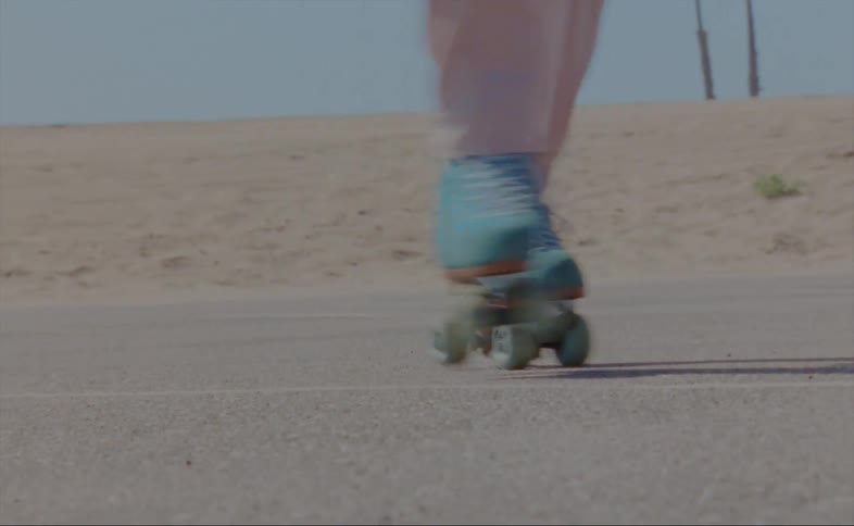 A man wearing pink pants is dancing on blue roller skates and showing off fancy footwork