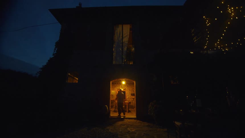A man walks in to a house and sets something on a table