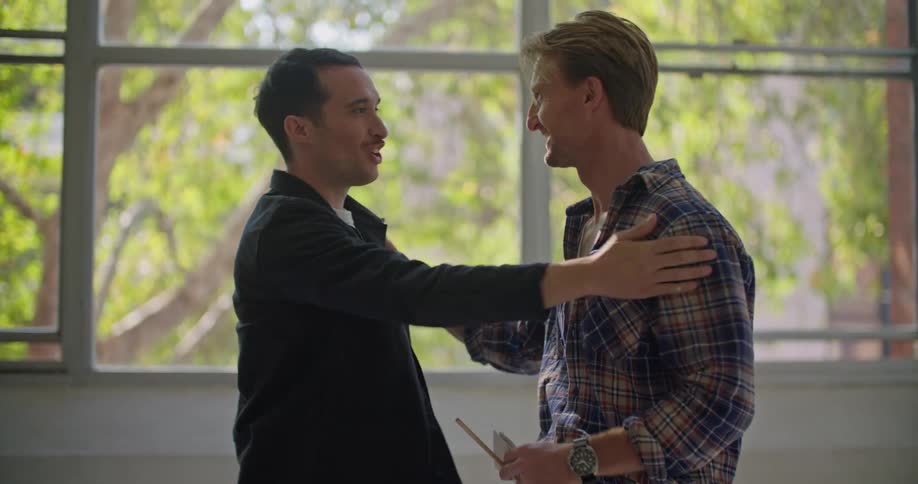 A pair of smiling men shake hands and pat each other on the shoulder before walking out of frame together