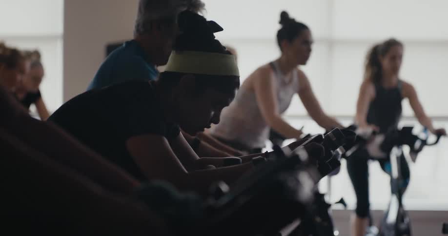 A group of people work out together on exercise bikes indoors during the day