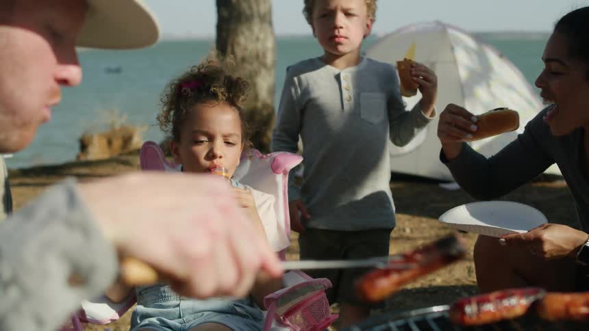 Dad serves hotdogs off the campsite grill for his happy family