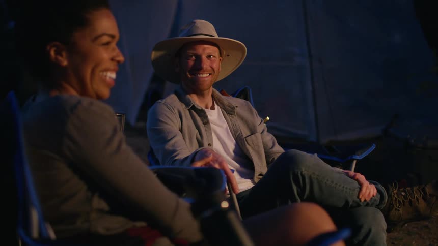 Two people sit by the tent talking