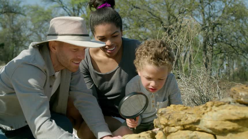 Man points an interesting spot on a rock for a kid to look at with a magnifying lens