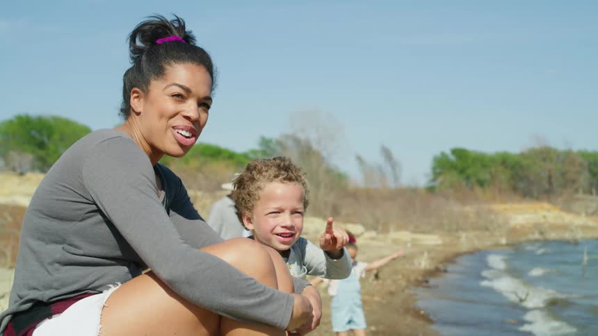A woman is sitting along the coast with her little boy as waves roll into shore