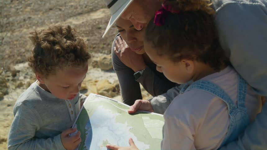 A family looks at map in a map book together while standing outdoors during the day