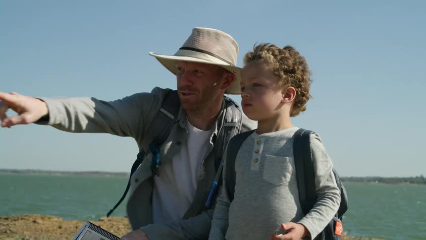 A bird flies behind a father and son by the shore