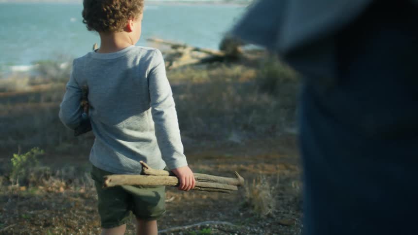 Boy helps his father to pick up wood near the coast at morning